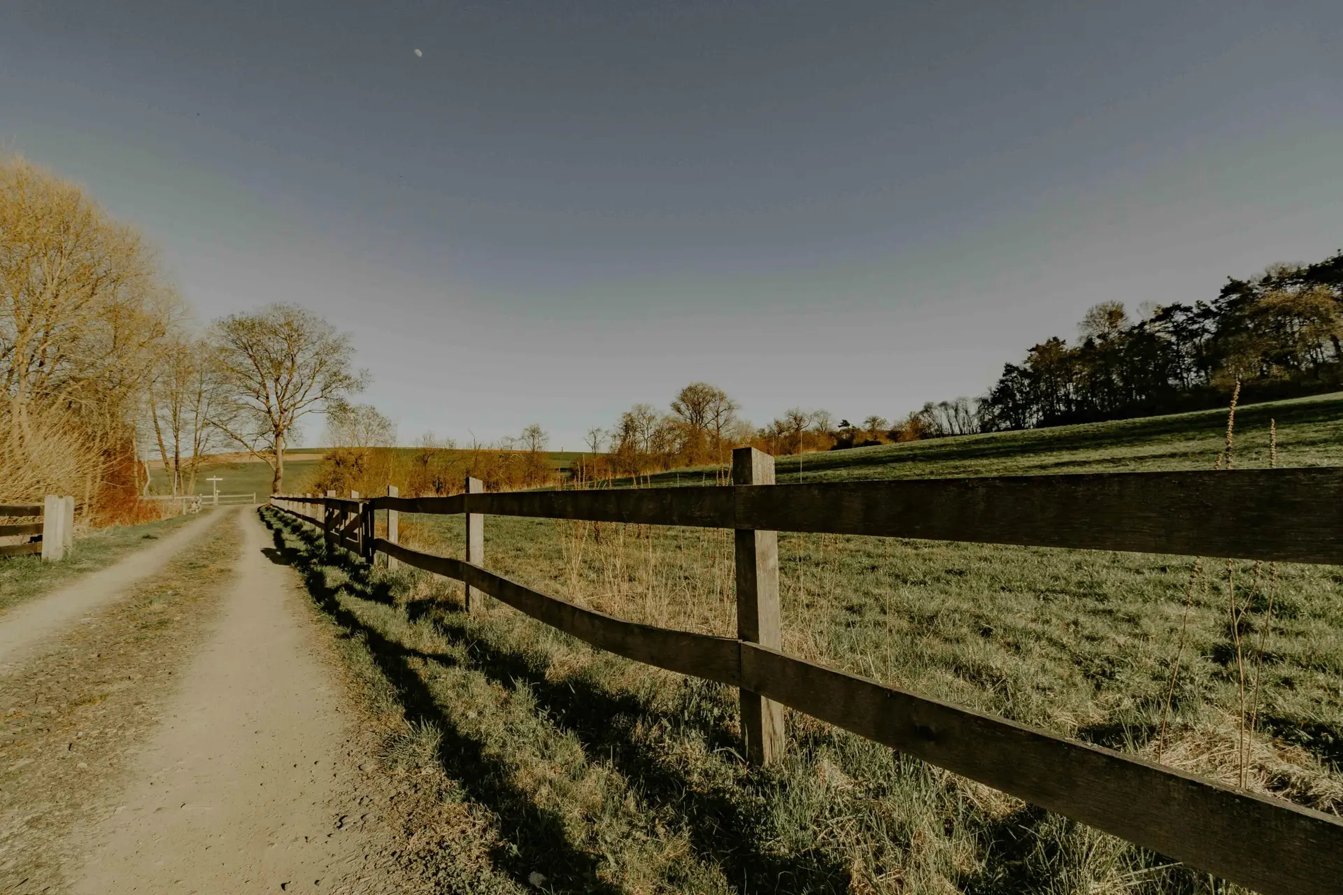 Tranquil landscape showcasing a rustic path beside a wooden fence at golden hour.
