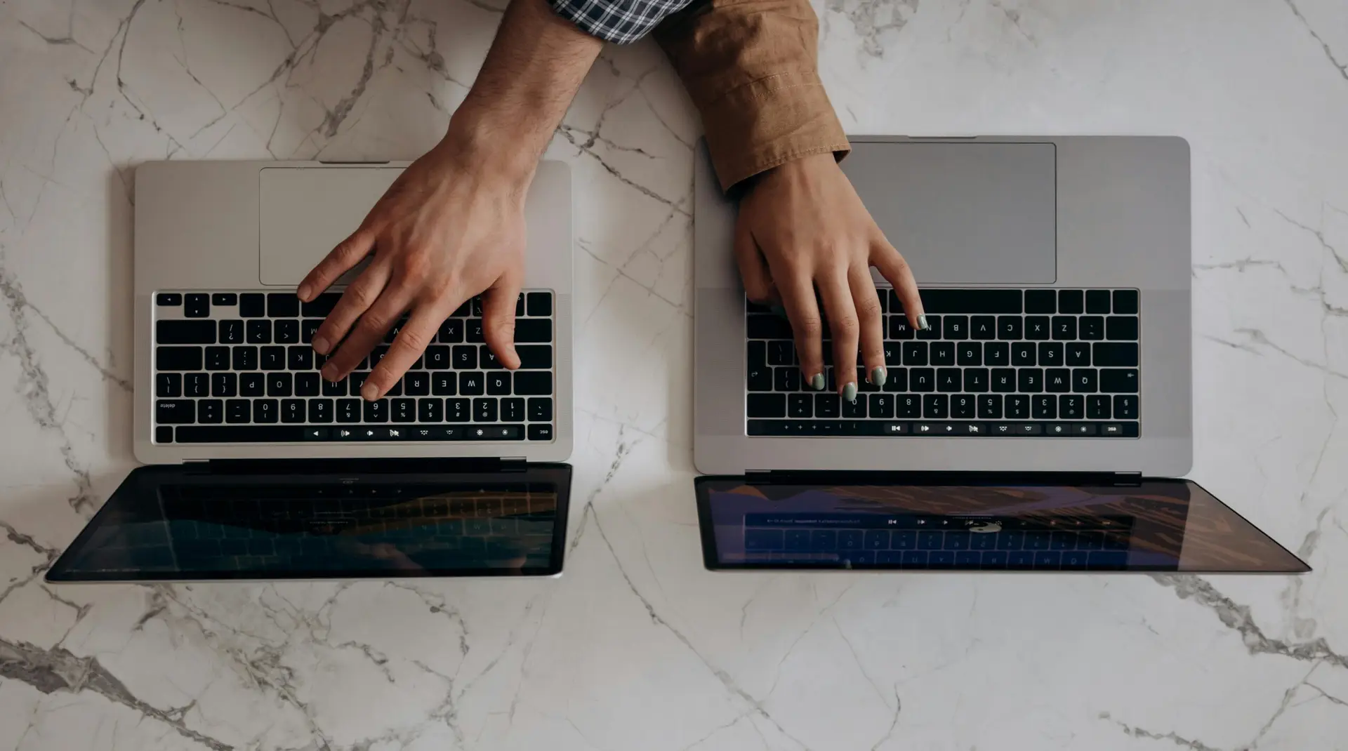 Two individuals typing on laptops from a top view angle, showcasing collaborative work.